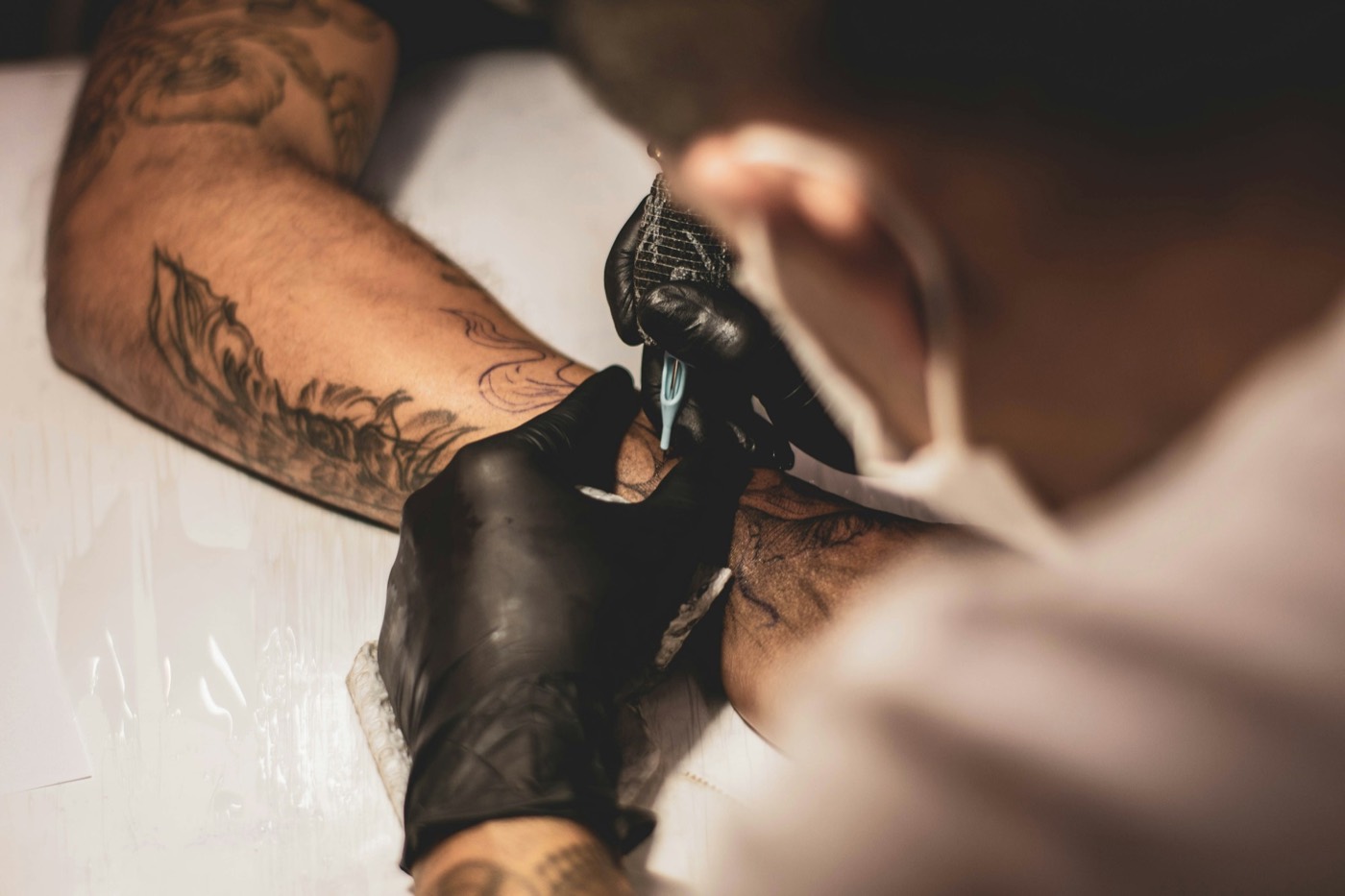 An artist in black gloves tattooing a client's forearm.