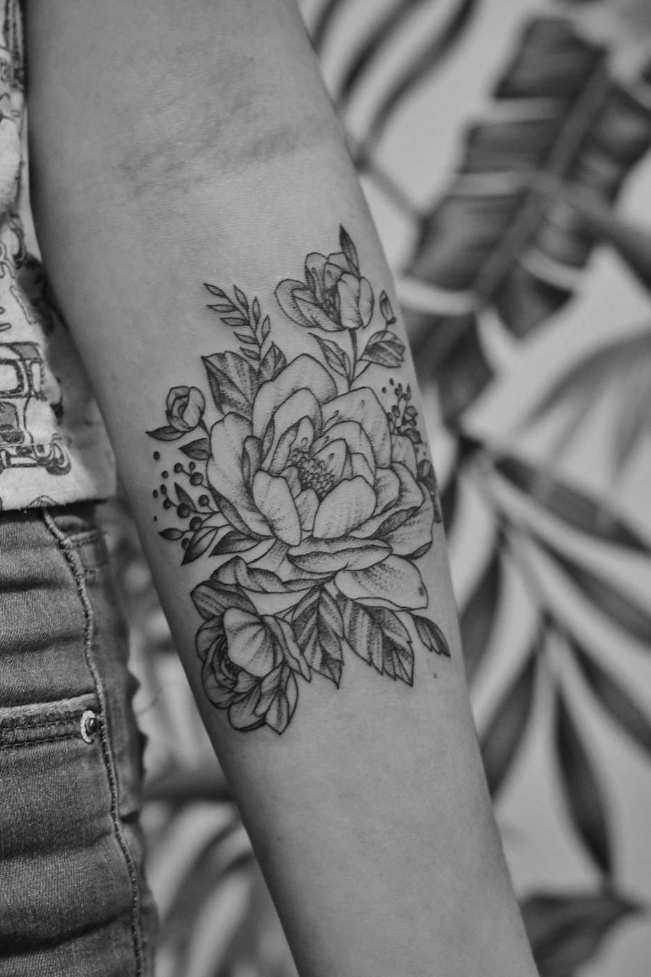 A fine-line flower tattoo on a forearm, in black and white.