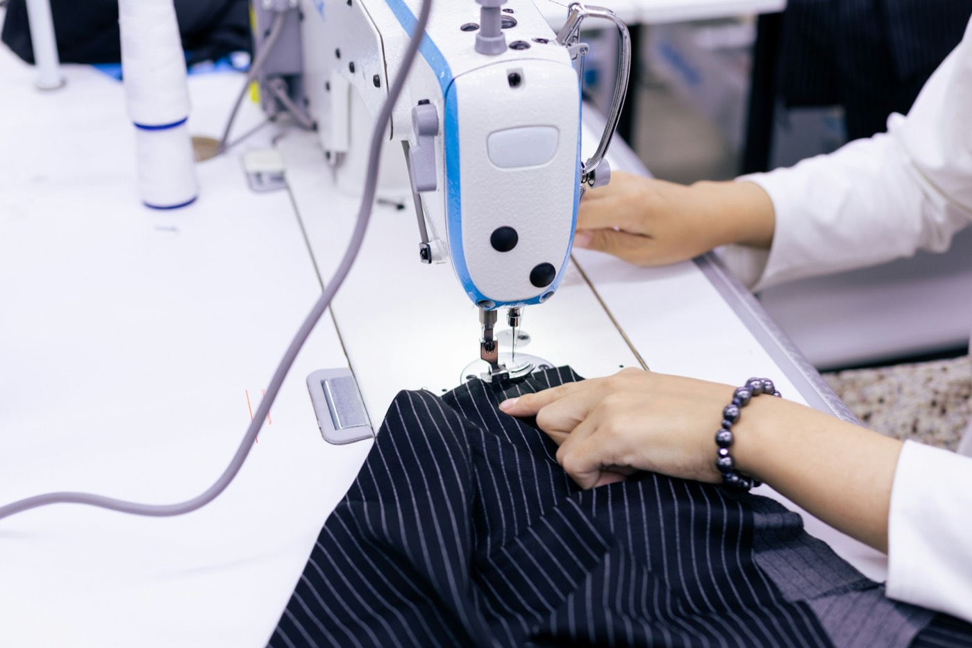 Hands guiding pinstripe fabric through a sewing machine