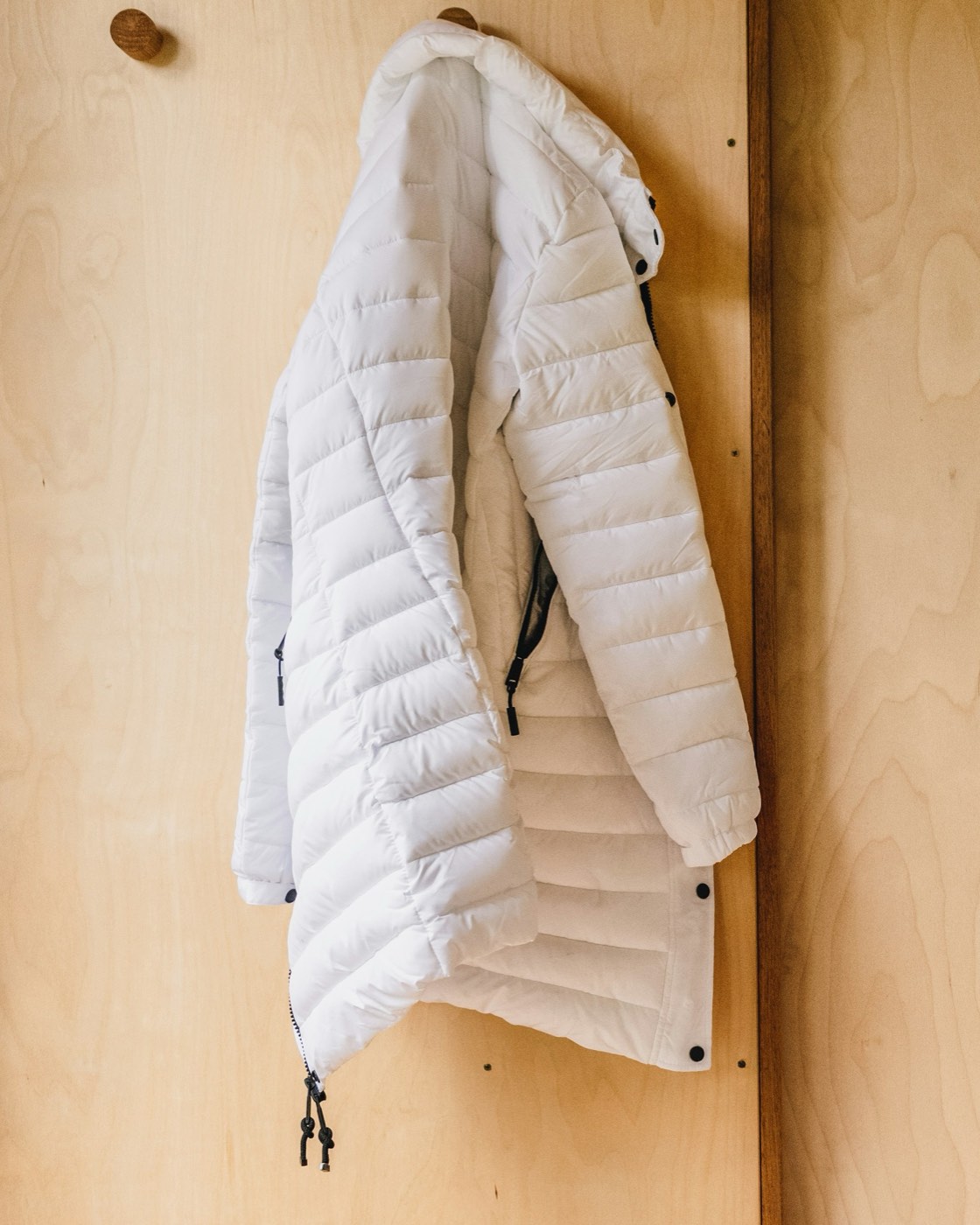 A white hooded down coat hanging on a wooden wall