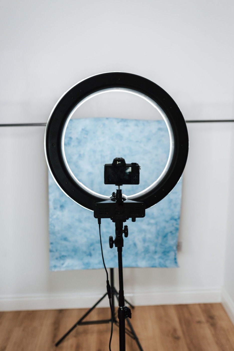 A camera inside a ring light on a tripod, aimed at a blue backdrop