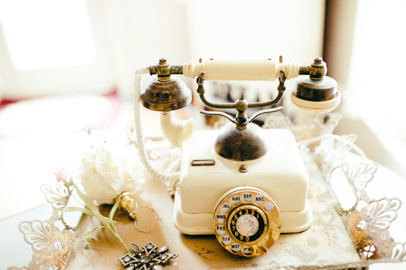 A white vintage rotary telephone on a tray beside a white flower