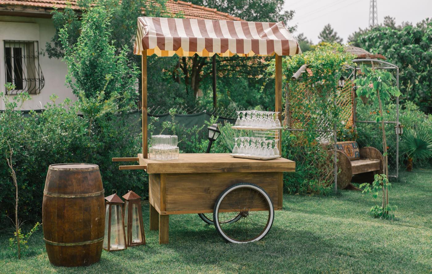 Wooden serving cart with a striped canopy and glassware on a garden lawn