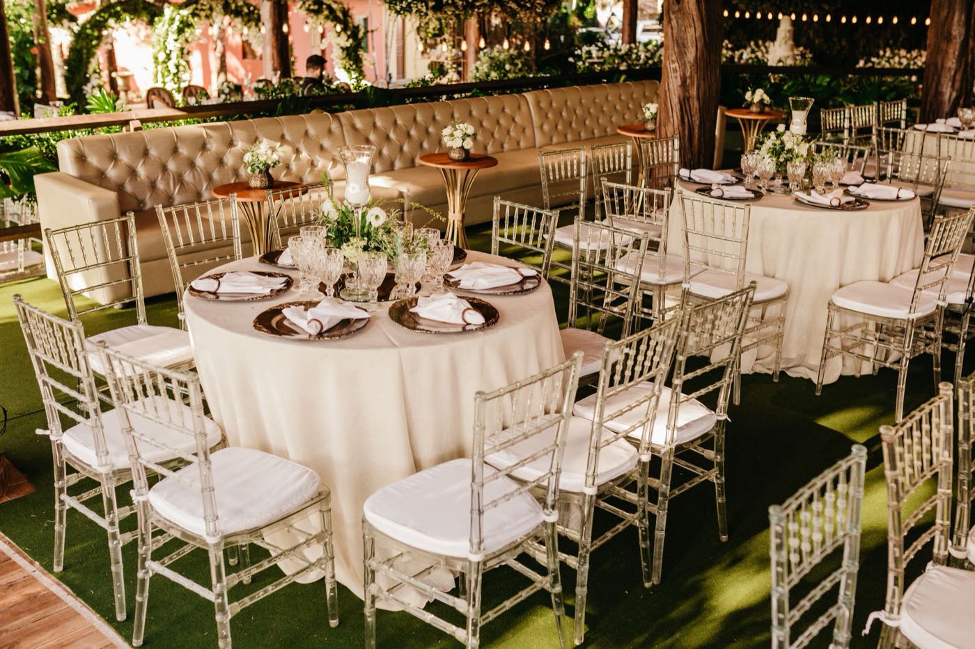Round tables in ivory cloths with clear chairs and white cushions, set for a reception