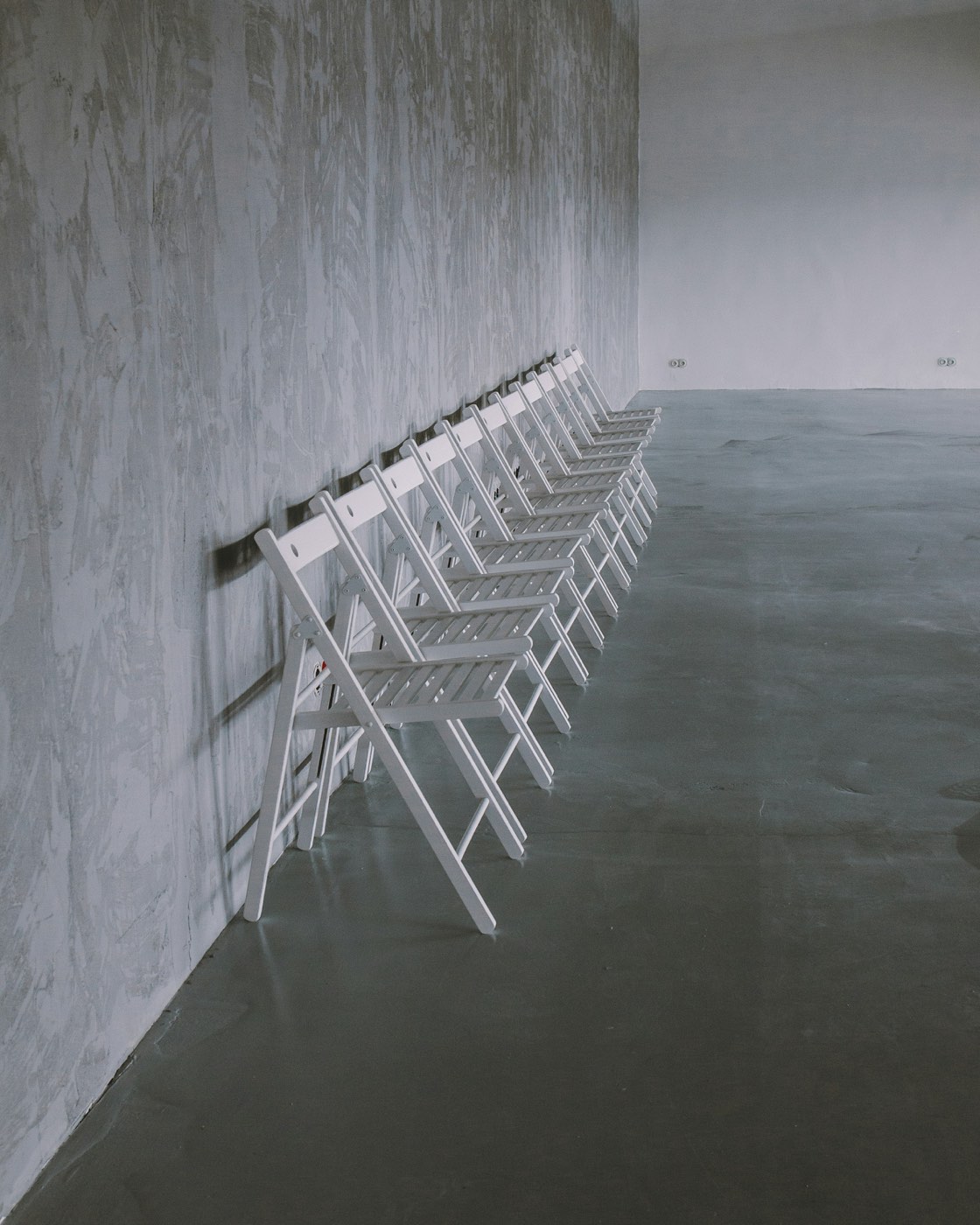 White wooden folding chairs folded and leaned in a row along a gray wall
