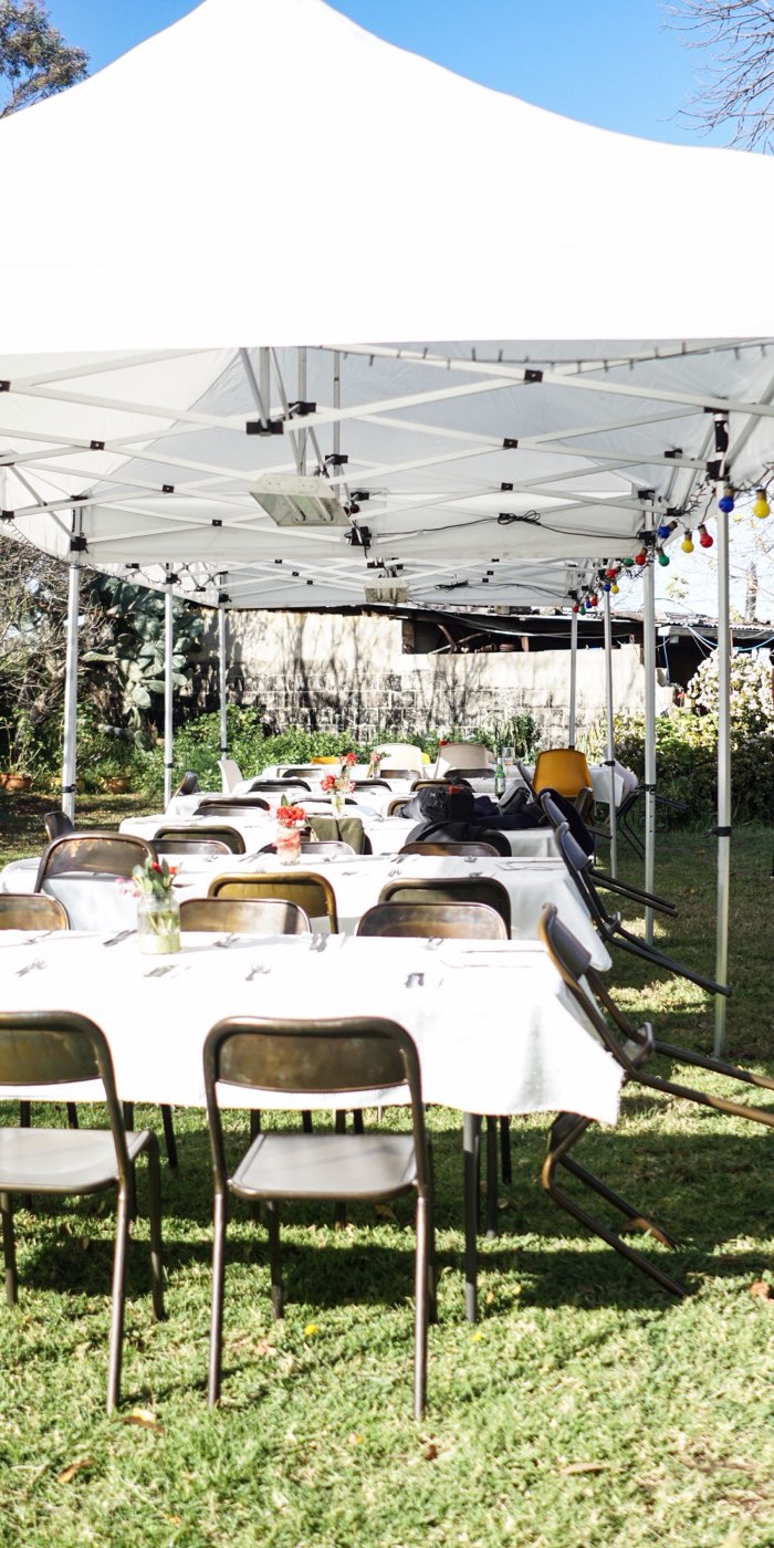 Rows of tables in white cloths with folding chairs under a white pop-up tent on a lawn