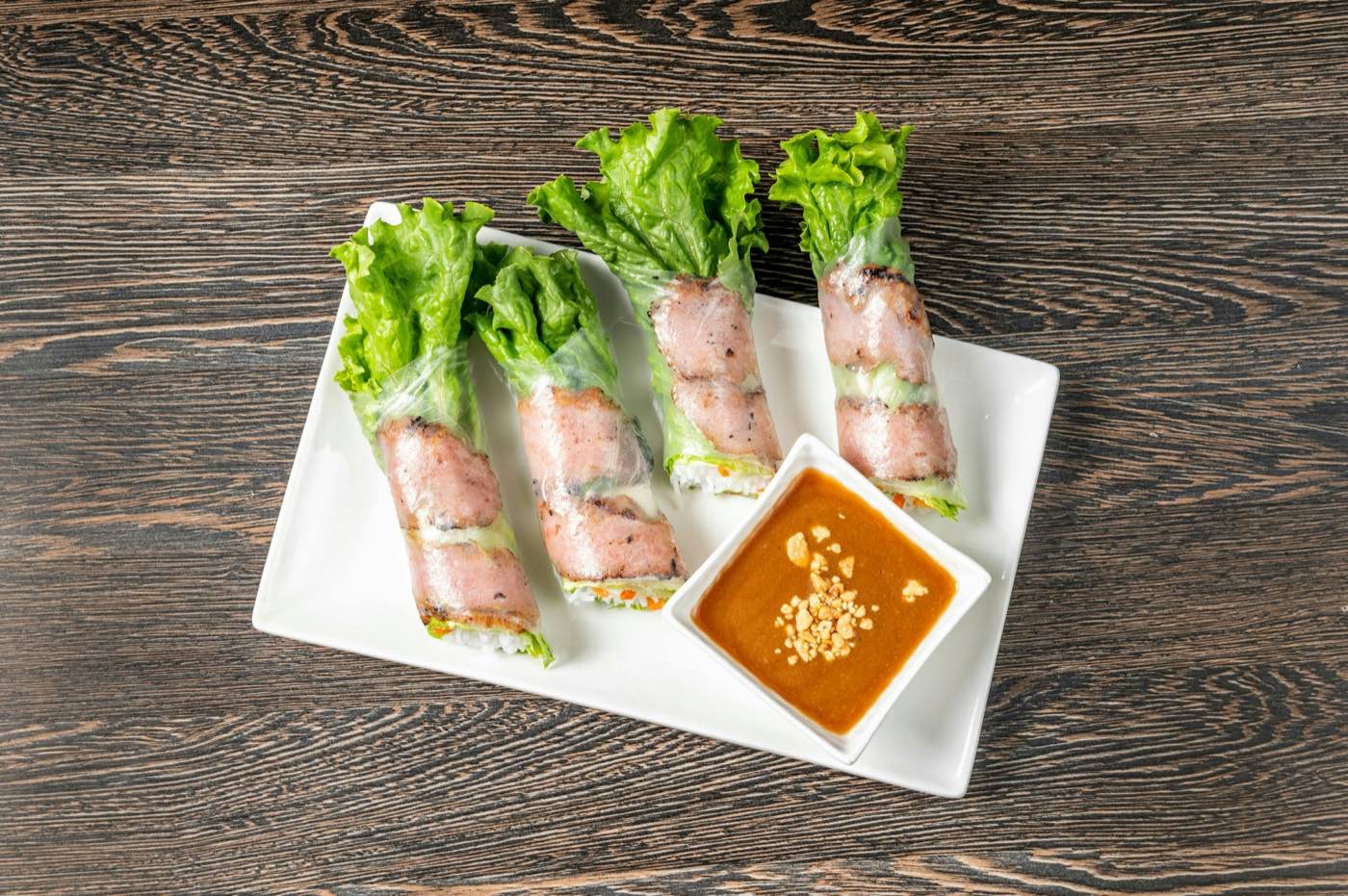 Fresh spring rolls wrapped with lettuce on a white plate, with peanut dipping sauce