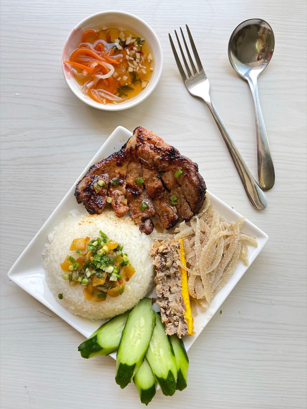 A broken rice plate with a grilled pork chop, scallion oil, cucumber and a small bowl of dipping sauce