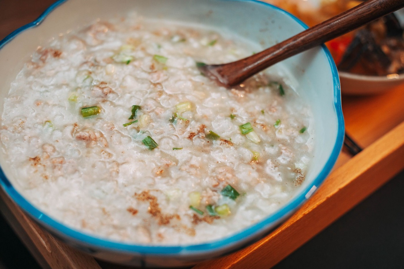 A bowl of rice porridge topped with scallions, with a wooden spoon