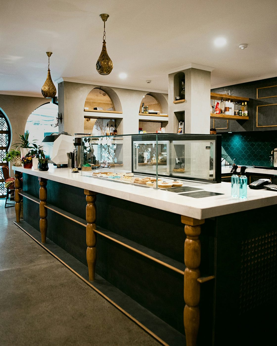 A cafe counter with a glass pastry case, an espresso machine and pendant lamps