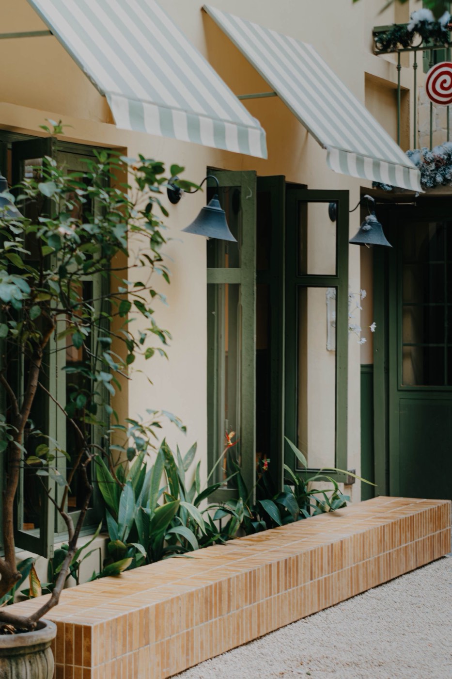A small cafe front with striped awnings, wall lamps and plants