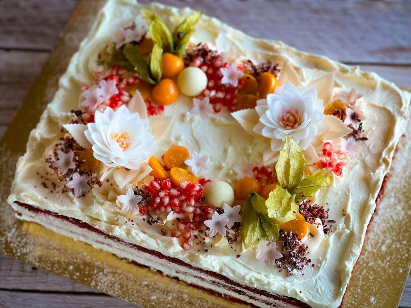 Rectangular cake frosted with cream and topped with sugar flowers and fruit