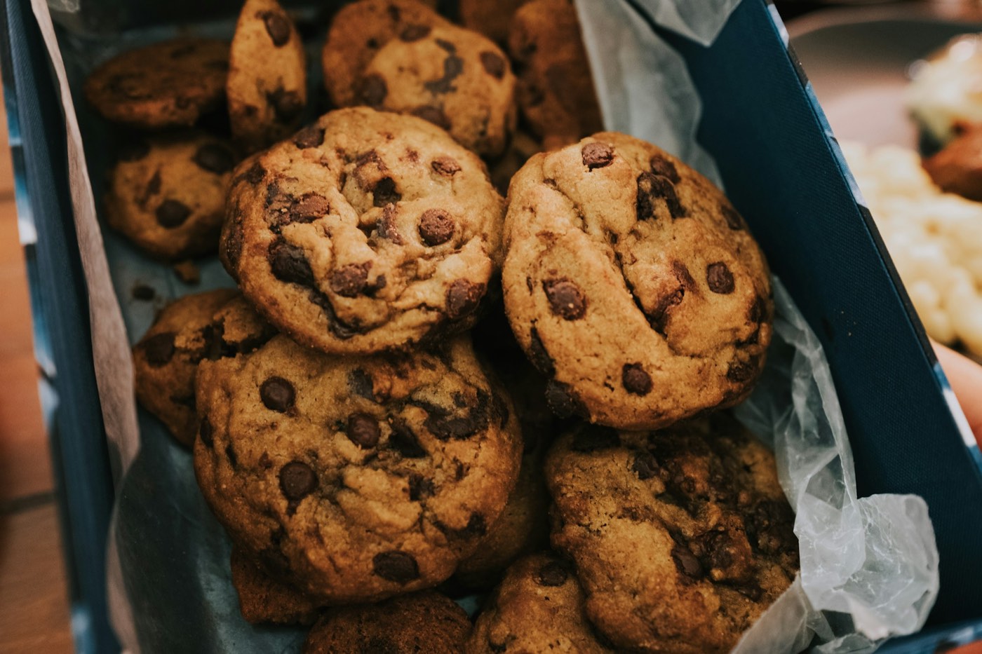 Chocolate chip cookies piled in a box lined with paper.
