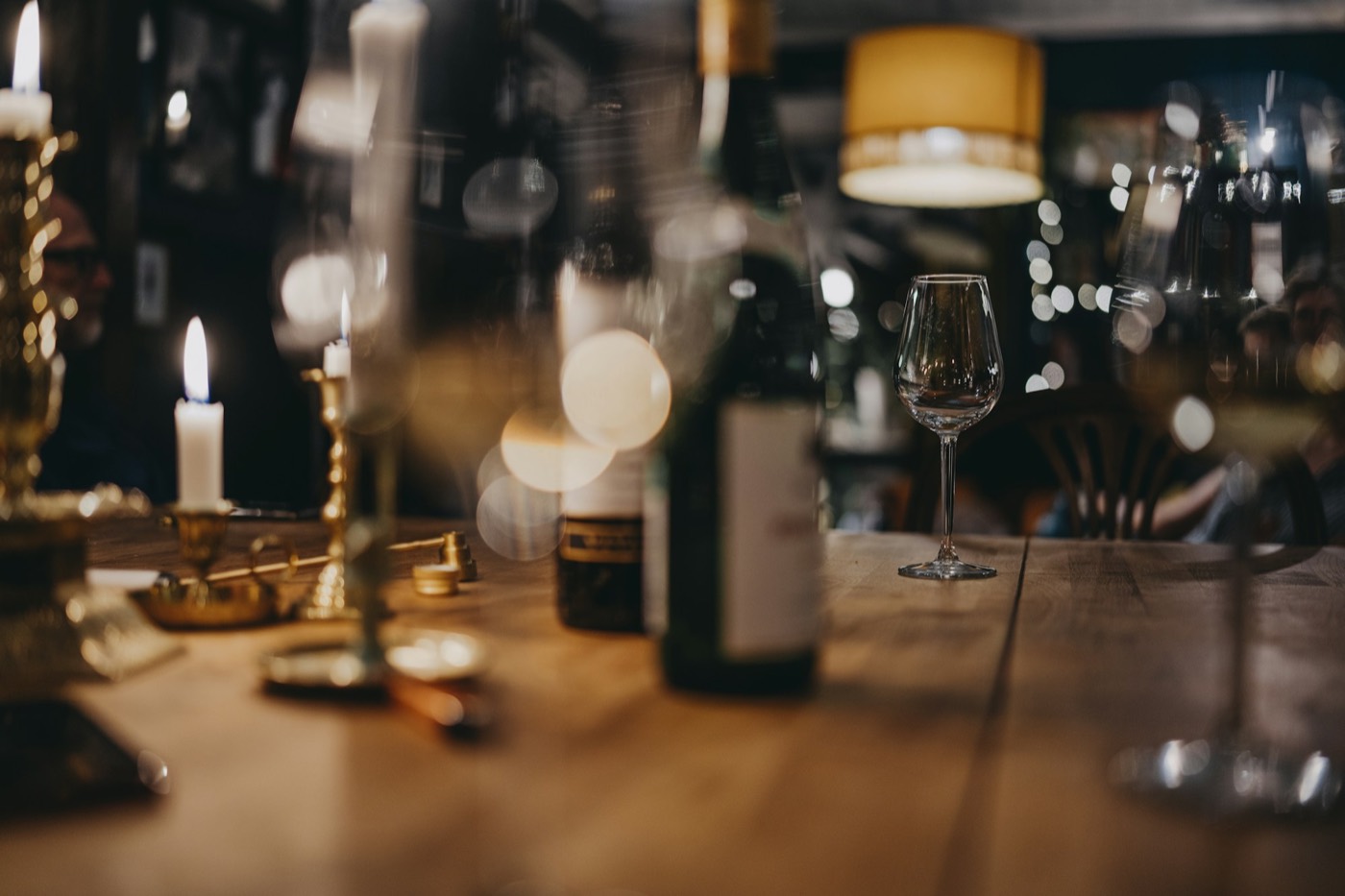 A candlelit table in a wine bar with a bottle and an empty wine glass, warm lights blurred behind.