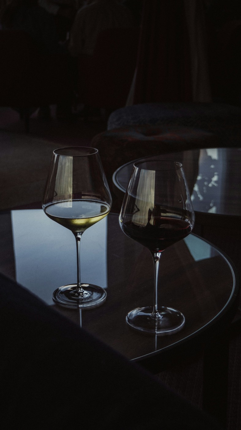 A glass of white wine and a glass of red wine on a dark glass table.