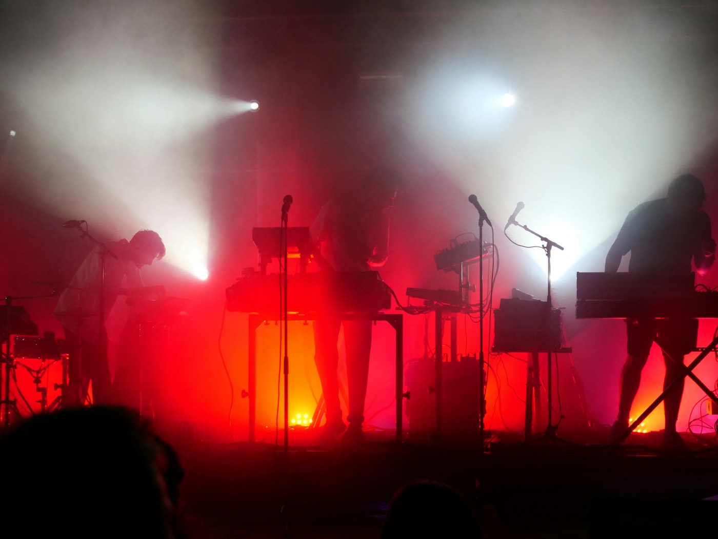 A band plays under red stage lights, seen from the crowd, the players in silhouette.