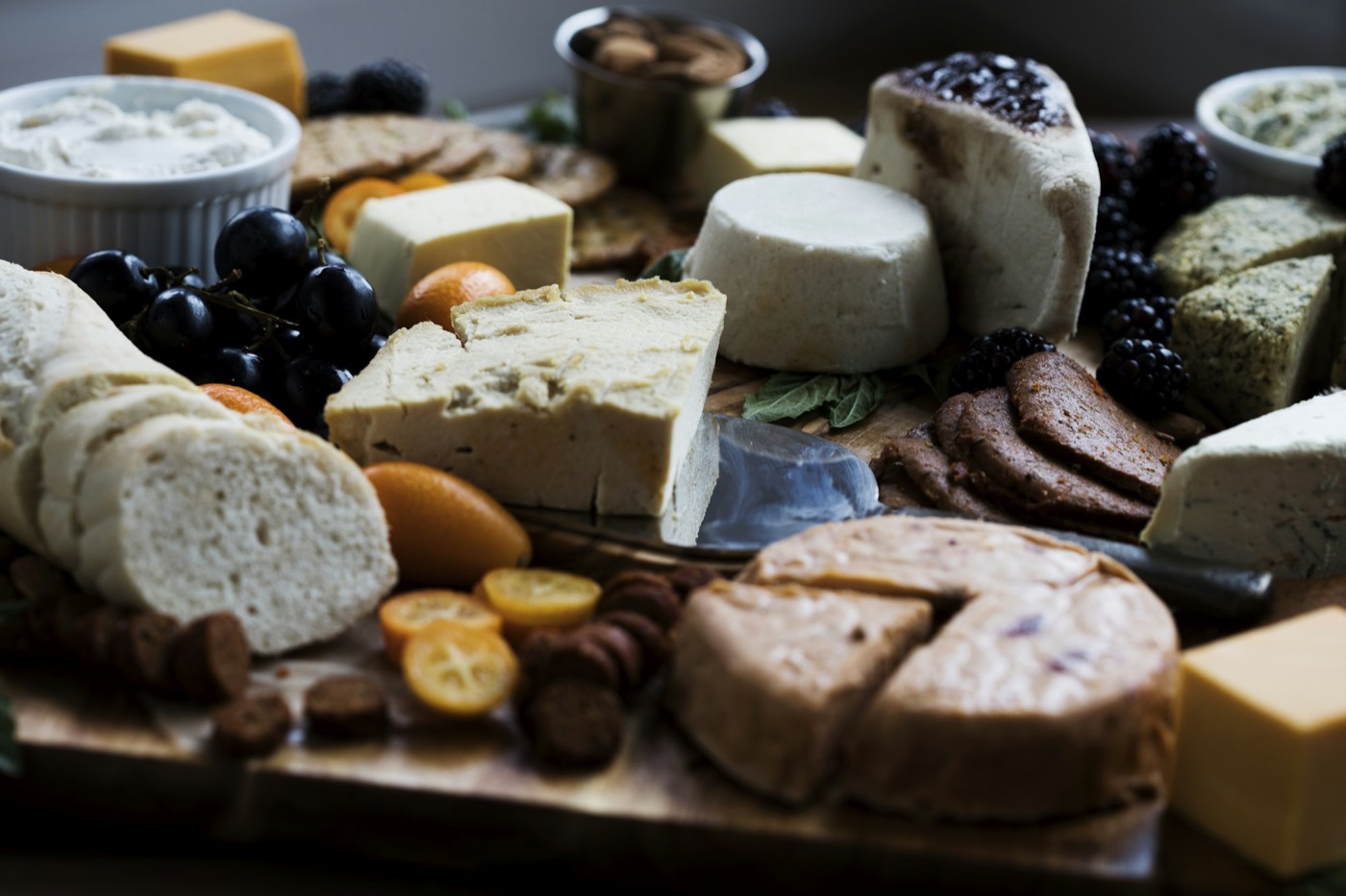 A cheese board with sliced bread, grapes, berries and small bowls of spreads.