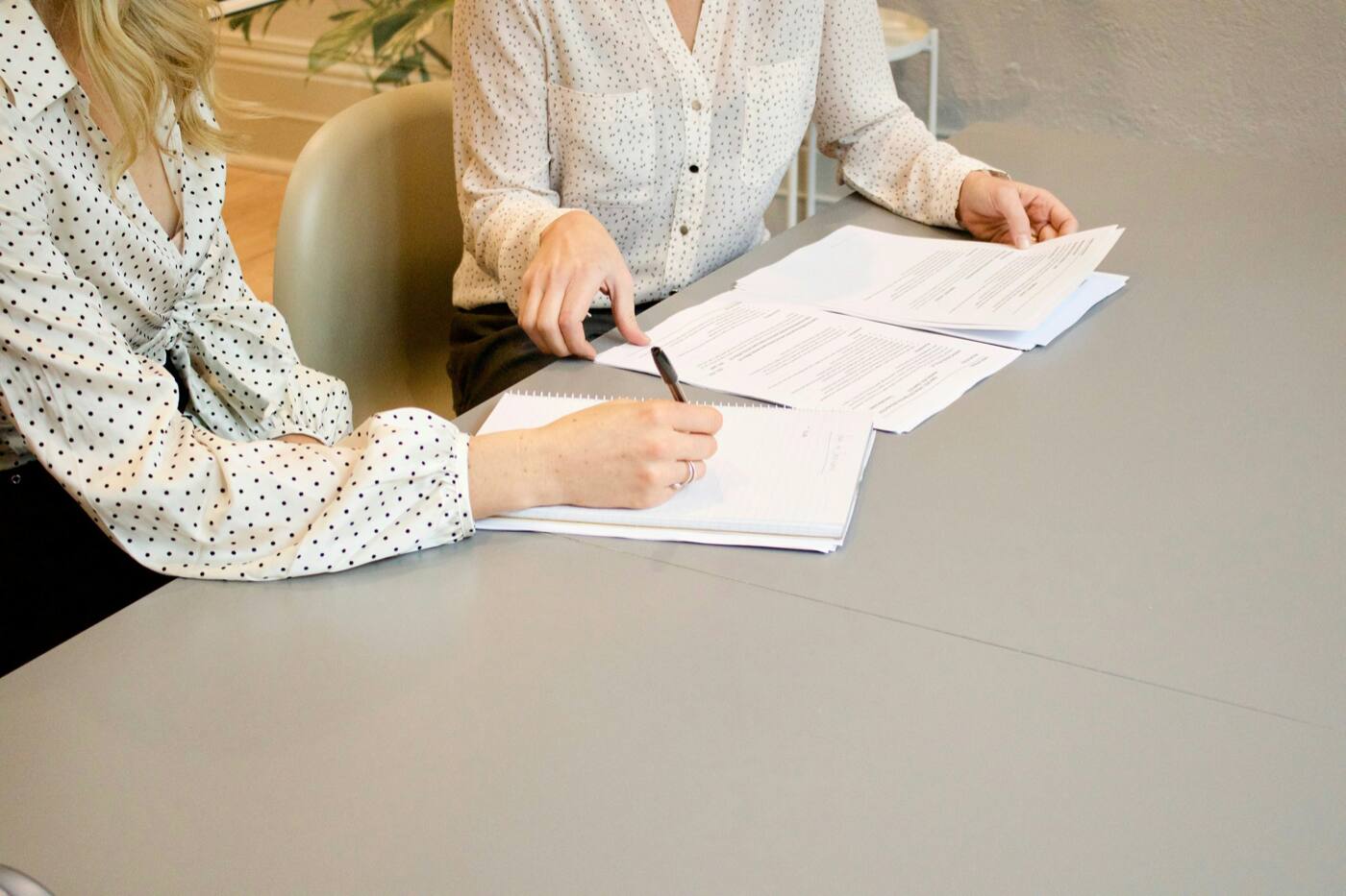 Two people at a gray table going over papers, one of them holding a pen