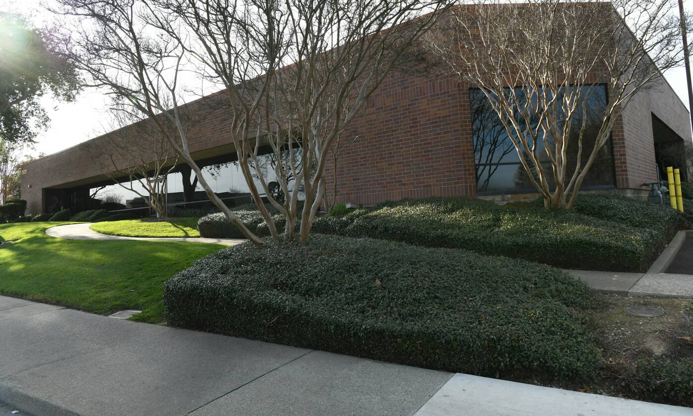 A one-story brick office building with dark windows, trimmed hedges and a small lawn.