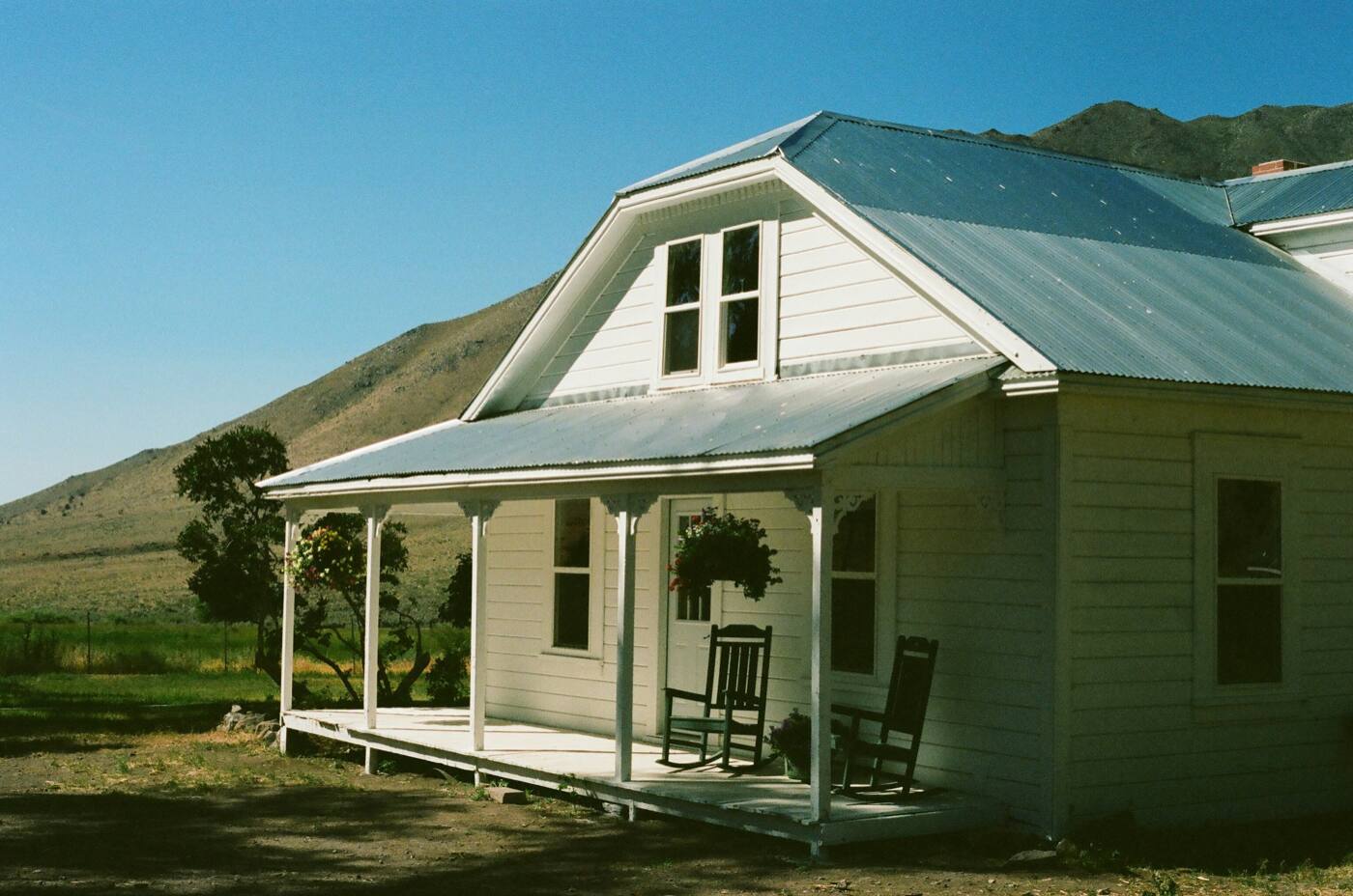 A small white farmhouse with a metal roof and a front porch with two rocking chairs