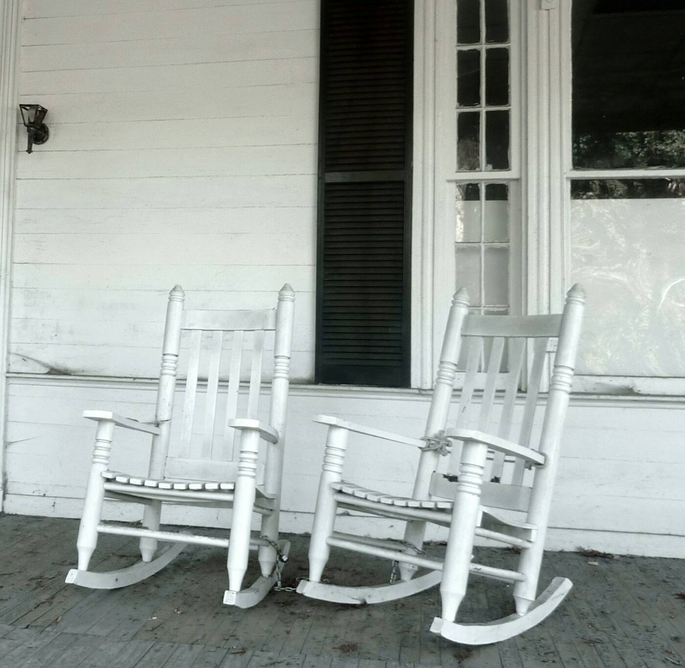 Two white rocking chairs on the front porch of an older white house