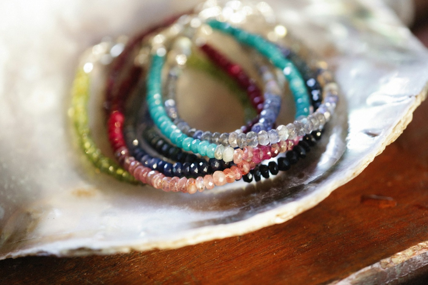 Stacked bead bracelets in pink, green, navy and red resting in a shell