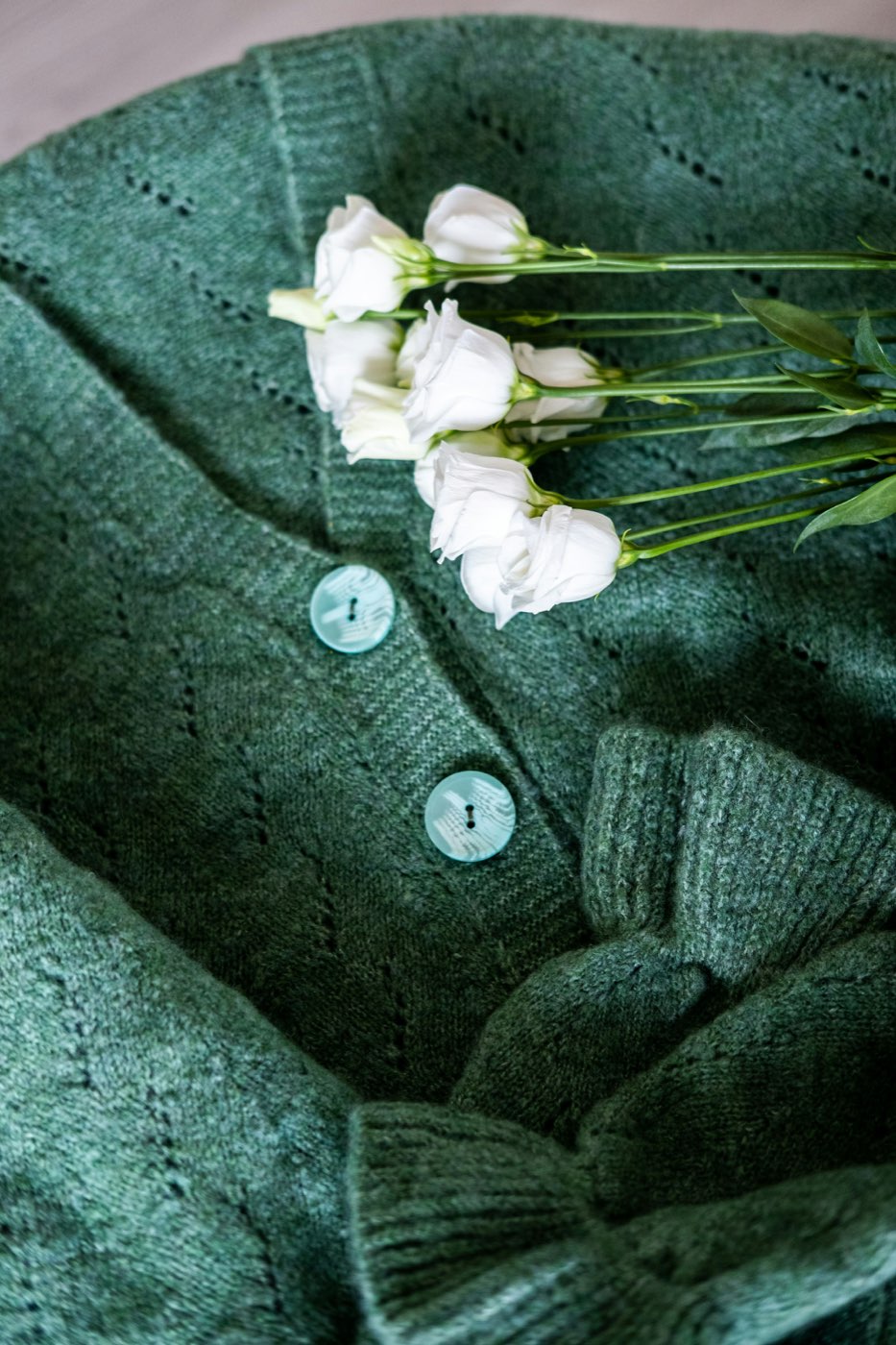 A folded green knit cardigan with white flowers laid across it