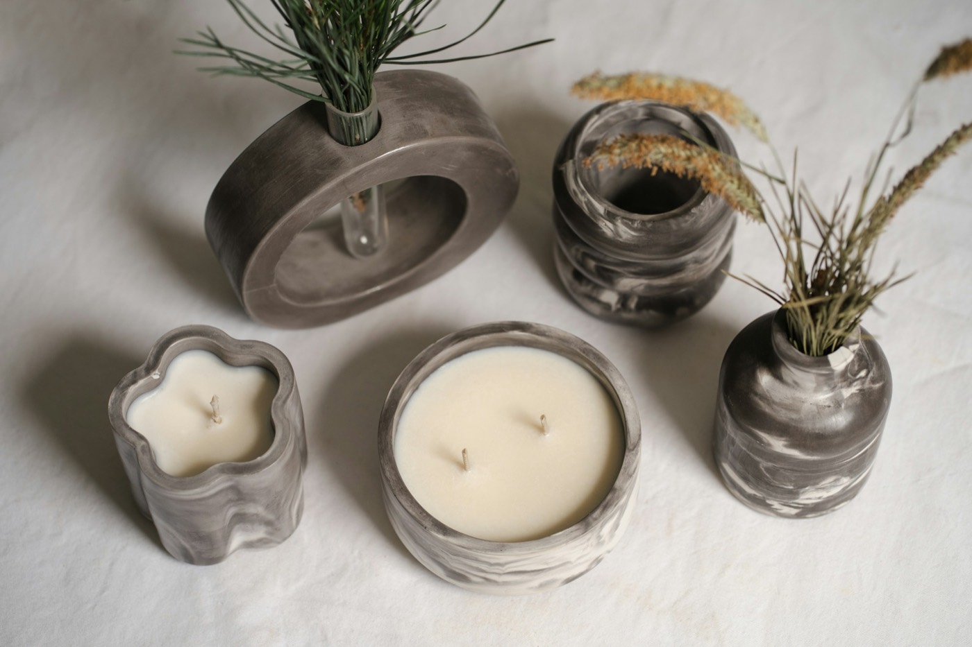 Candles in marbled jars beside small vases of dried grass