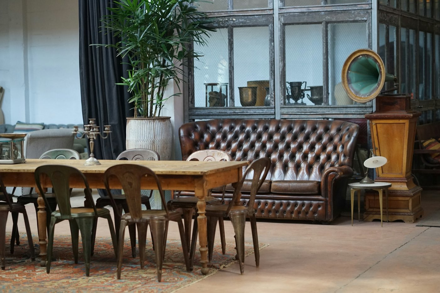 A room of vintage furniture with a tufted leather sofa, a long wood table and metal chairs