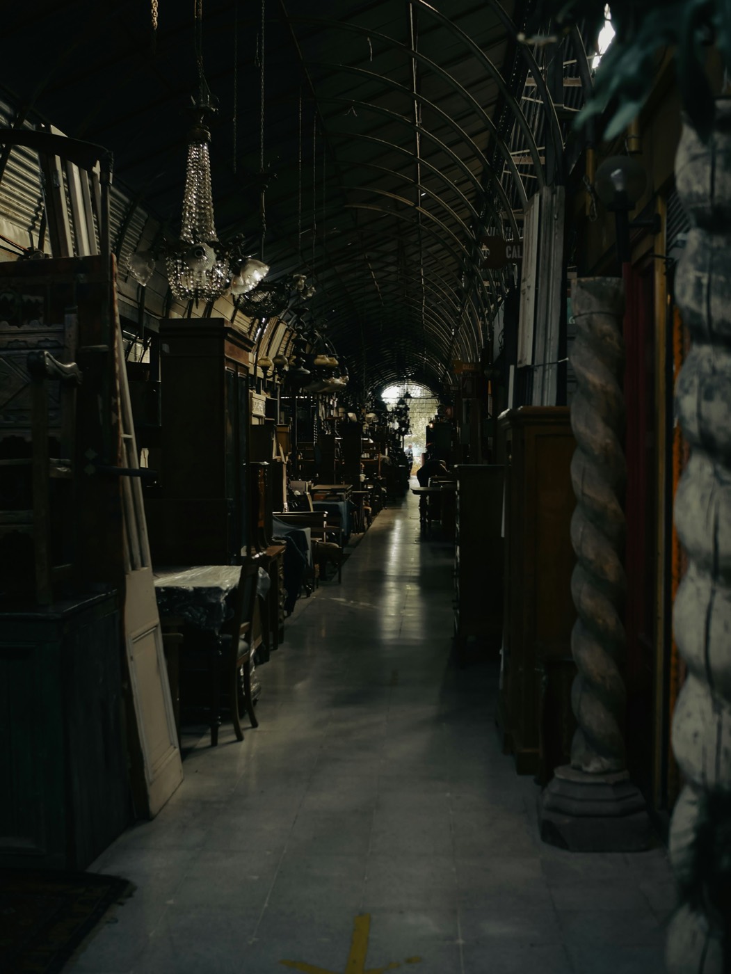 A long aisle lined with antique wardrobes, tables and hanging chandeliers