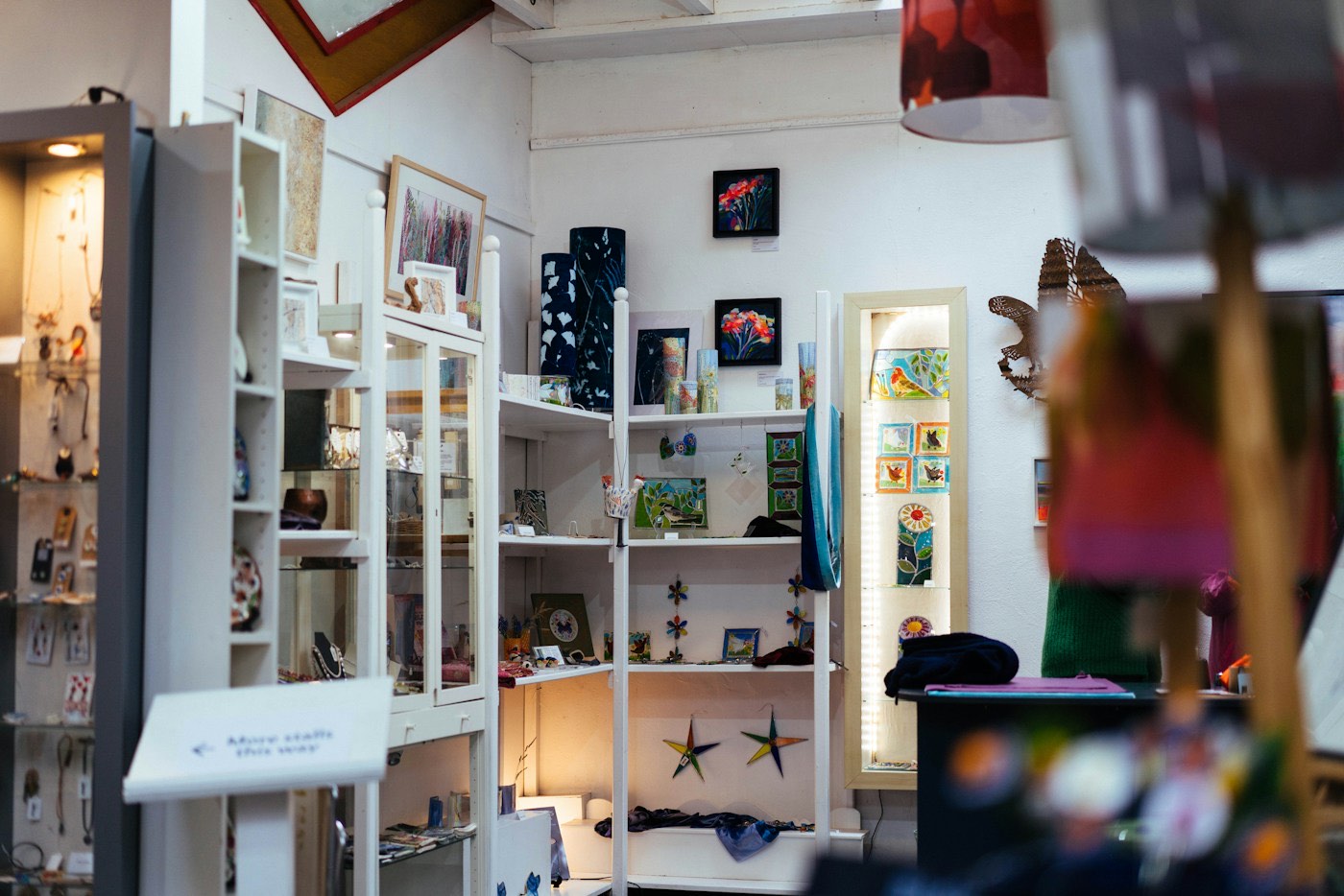 A small shop corner with white shelves of framed flower paintings, glass art and display cases