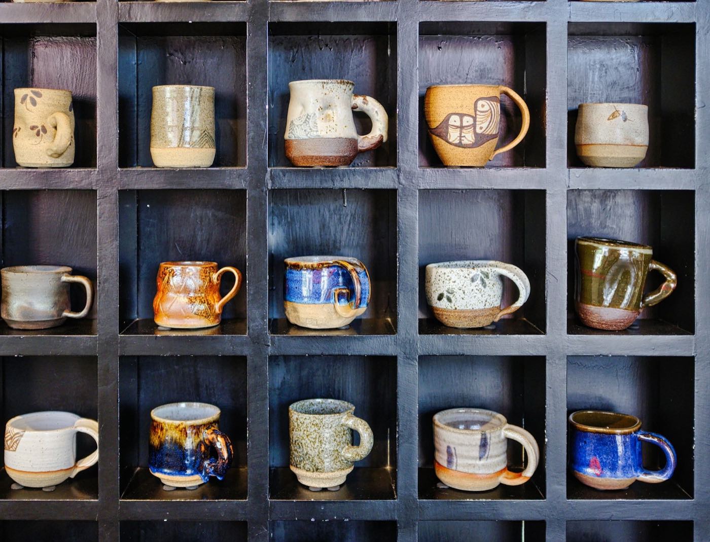 Handmade glazed mugs in blue, rust and speckled cream, one to a cubby on a black shelf