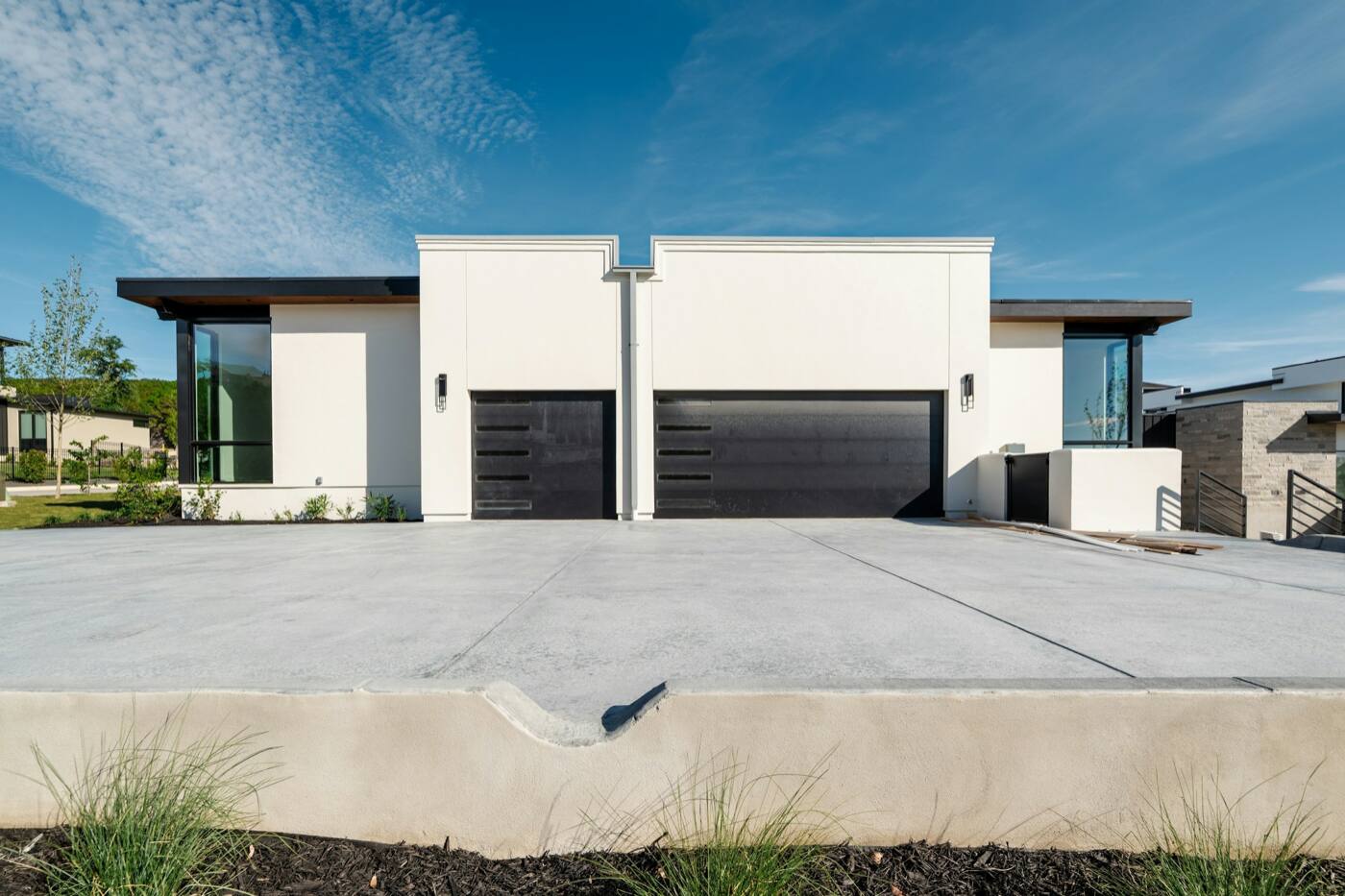 A white house with two dark garage doors behind a wide concrete driveway