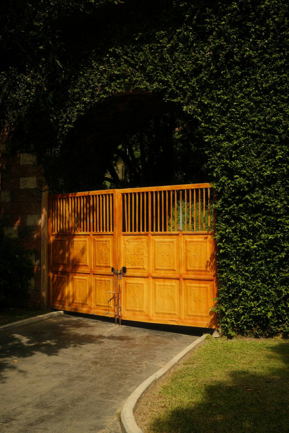 A wood double gate across a driveway, under an arch of ivy