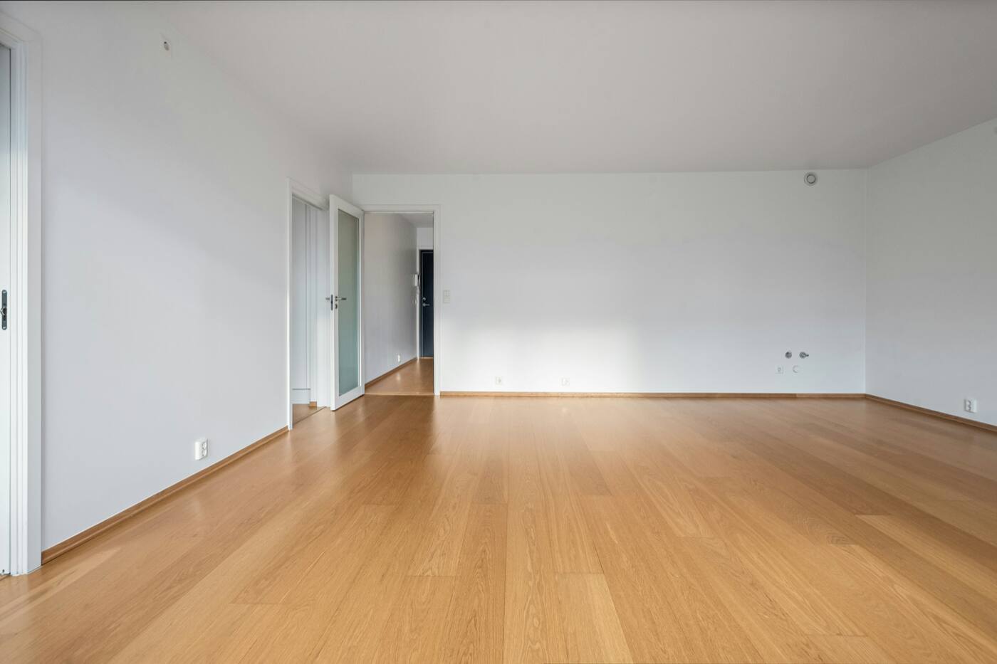 An empty open room with a light oak floor and white walls