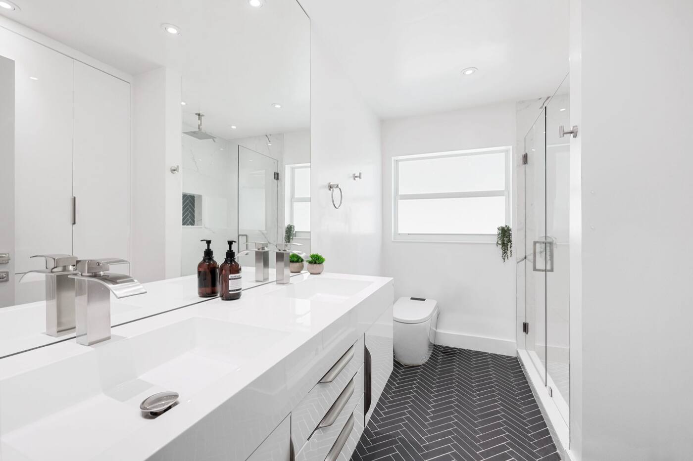 A white bathroom with a dark herringbone tile floor