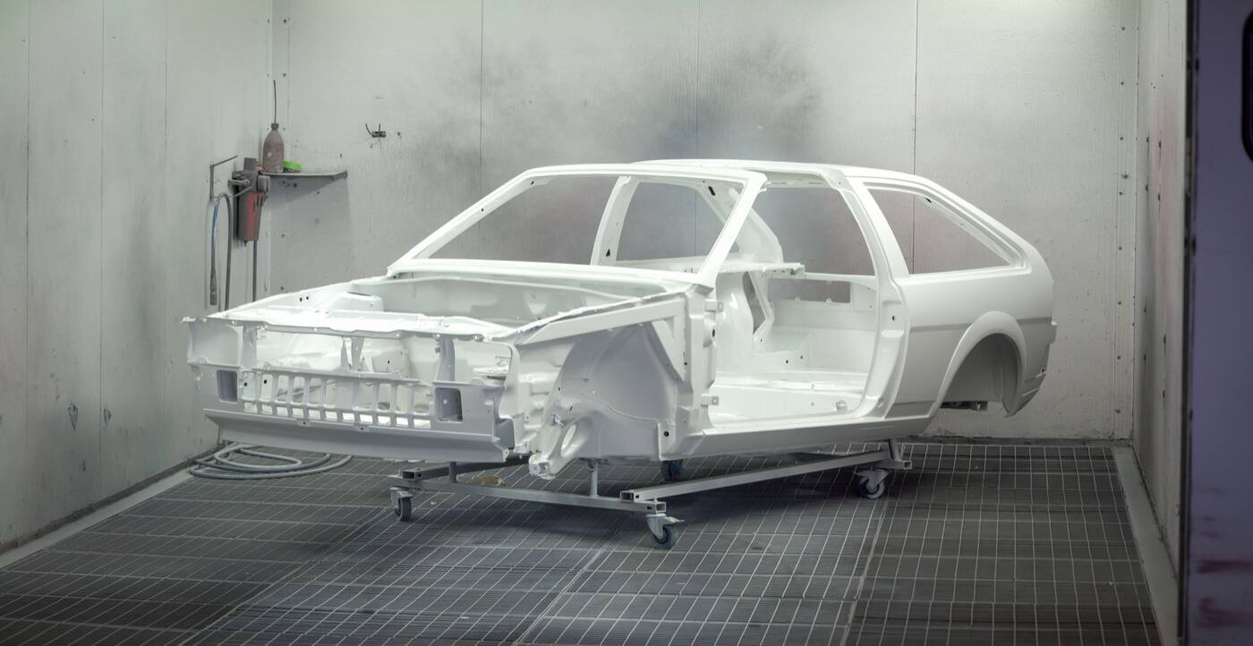 A bare car body painted white, on a stand in a paint booth
