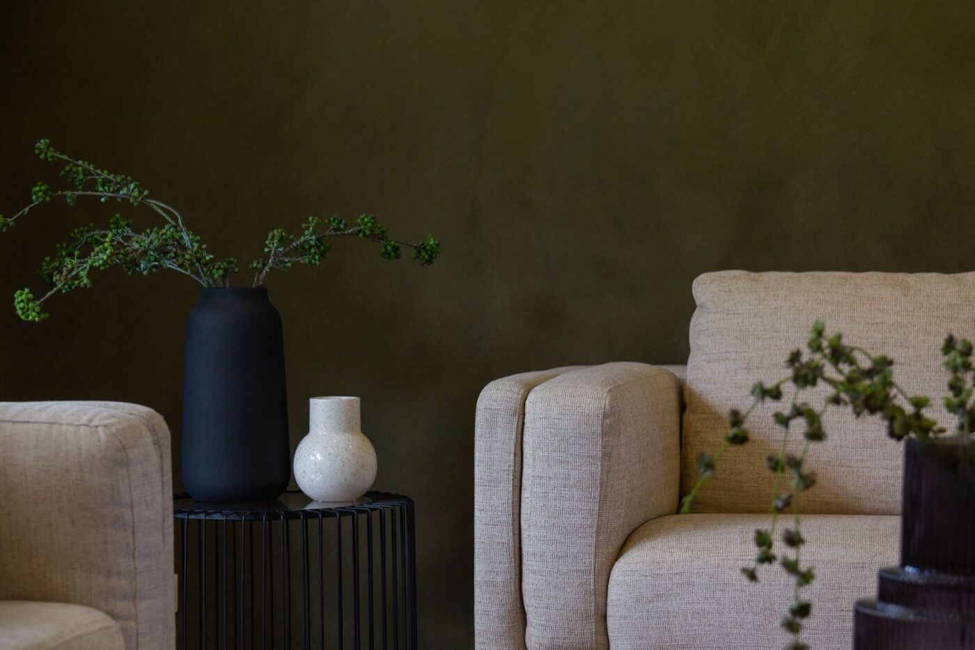 A living room wall painted deep olive green behind two cream armchairs